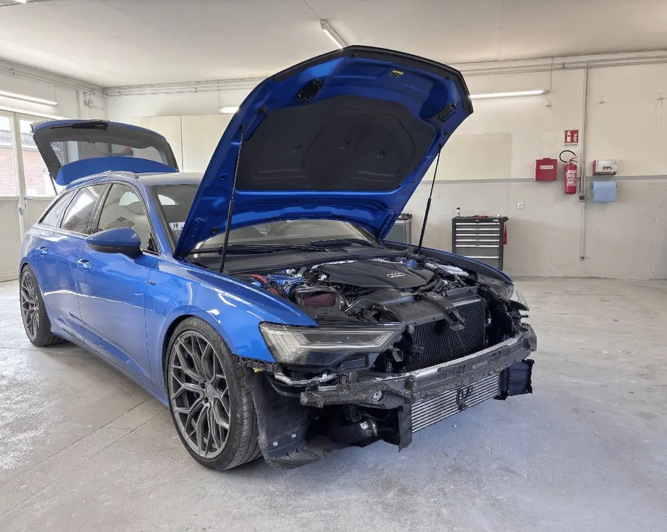 Blauer Audi mit geöffneter Motorhaube und Frontschaden in der Werkstatt